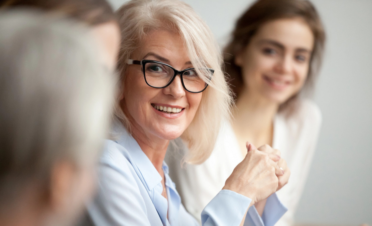 Older woman in glasses smiling at another coworker in a meeting